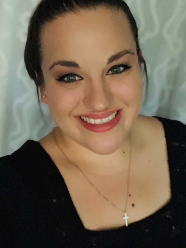 A woman with a Christian cross necklace and black dress smiles at the camera.